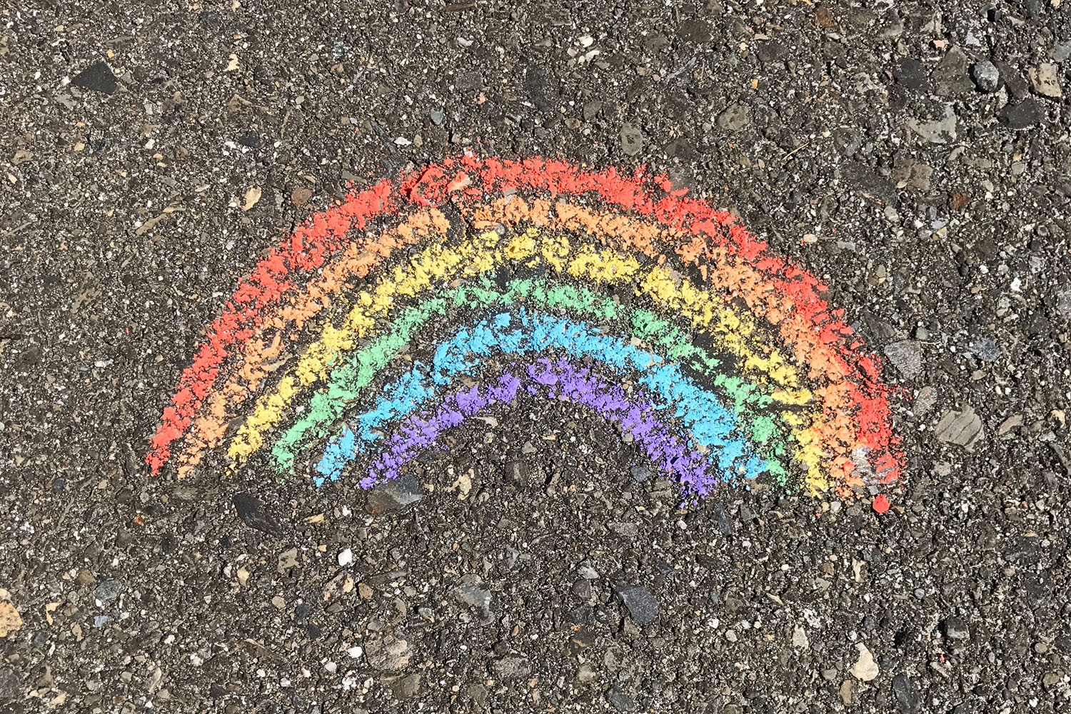 A colorful rainbow drawn in chalk on asphalt