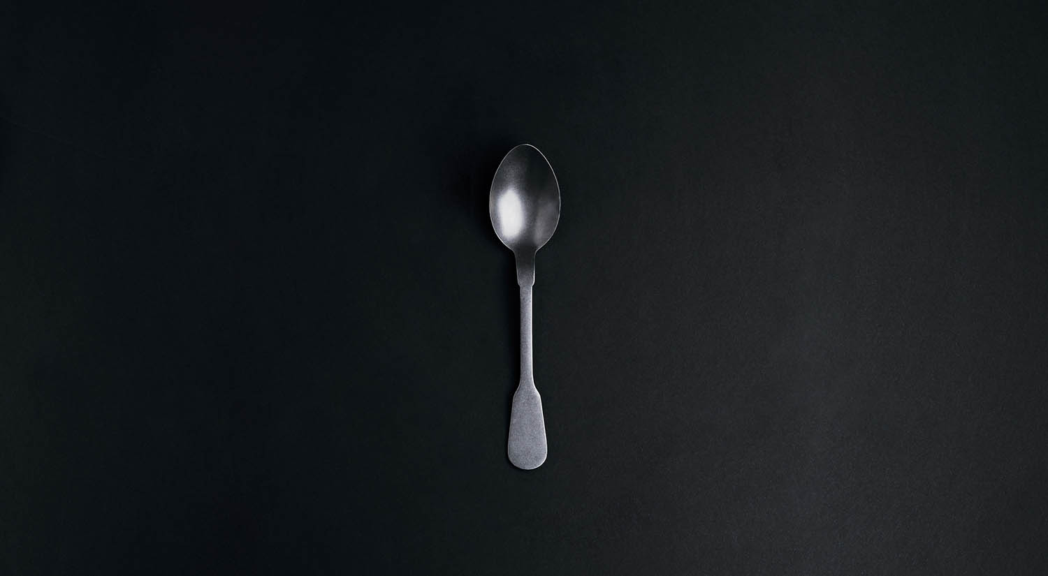 Raul Angel's photo depicts a single silver spoon resting on a black background. Sppons can represent units of energy for people with chronic illness. For that reason, chronically ill people often call themselves spoonies.
