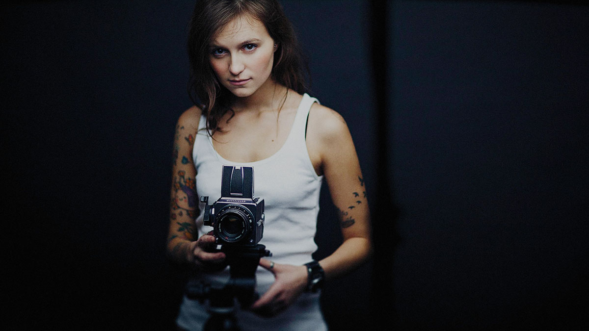 Alexey Demidov's photo of a woman in a white tank top holding a camera in a dark room highlights Anne SImone's article presenting content marketing examples for photography brands.